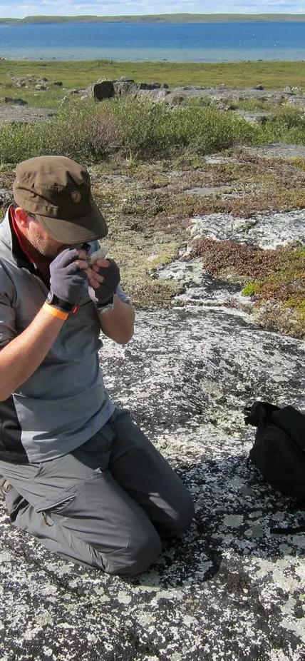 Graham Pearson using on of the field geologist's main tools, a simple hand lens, to look at the mineralogy of a rock during fieldwork at the Slave Craton, Canada.